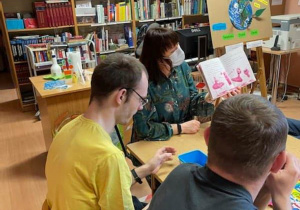 Pracownik Biblioteki Miejskiej w Radomsku pokazuje chłopcom ilustracje w książce podczas wizyty w bibliotece.