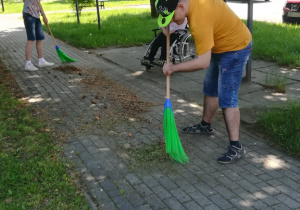 Dwóch chłopaków zamiata chodnik przez budynkiem internatu.