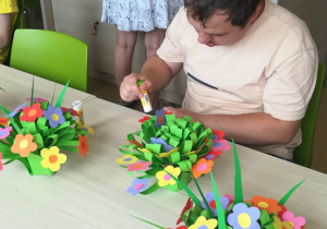 Uczestnicy Programu Rehabilitacja 25 plus wykonują bukiety kwiatowe z papieru.